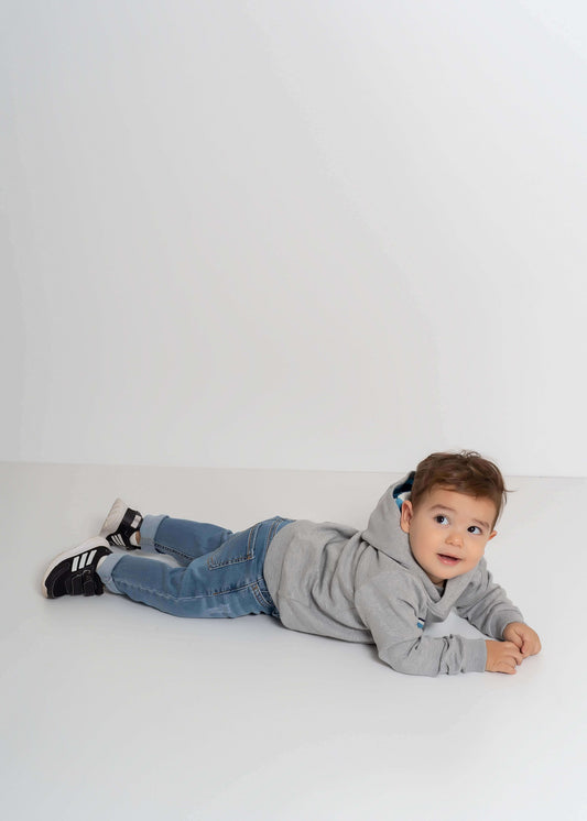Balıklı kapüşonlu sweatshirt giyen bir çocuk, yerde yatarken gülümsemekte, dikkat çekici balık nakışlarıyla.