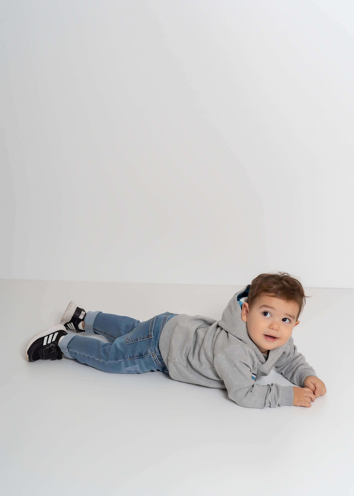 Balıklı kapüşonlu sweatshirt giyen bir çocuk, yerde yatarken gülümsemekte, dikkat çekici balık nakışlarıyla.