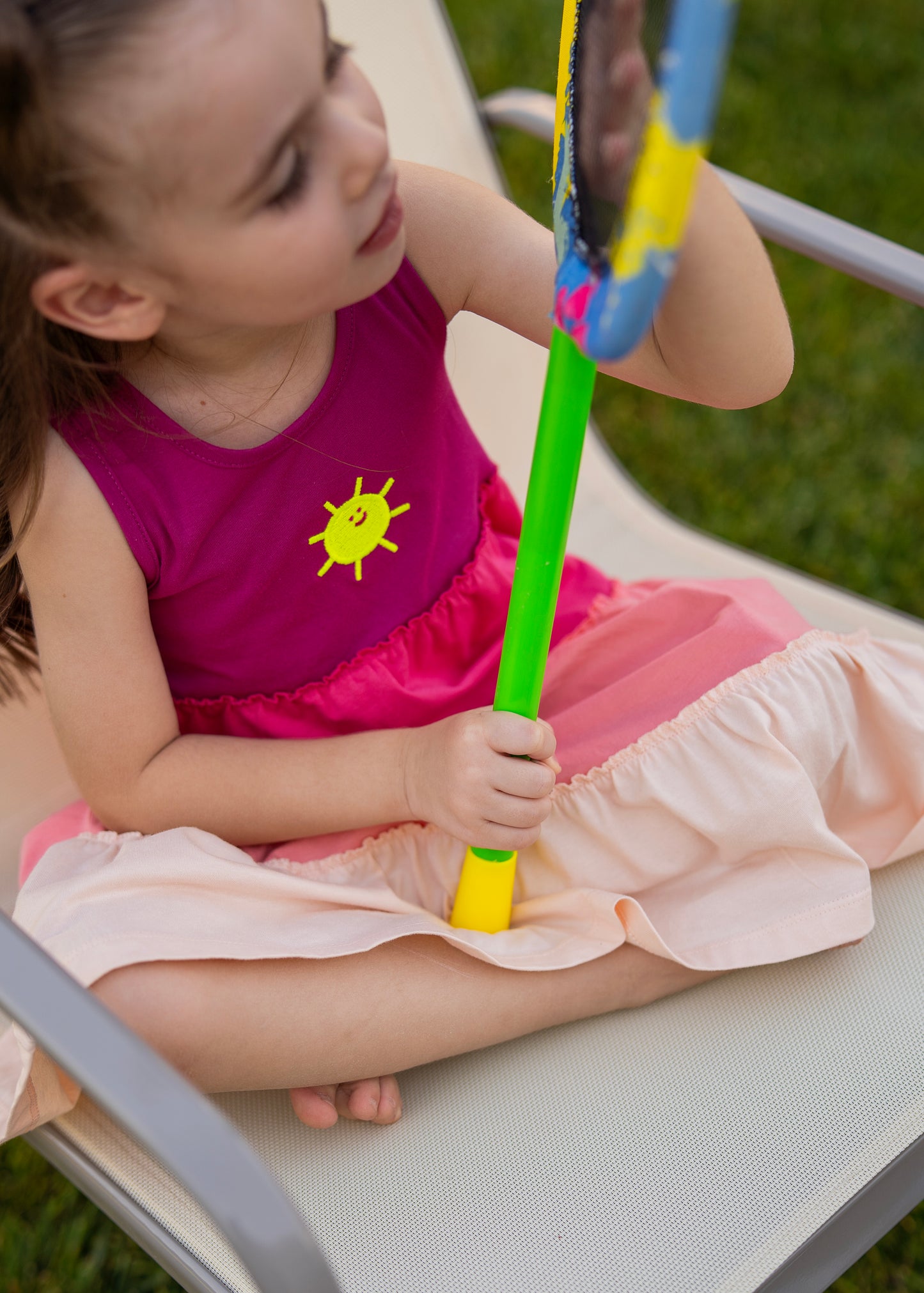 Child wearing a bright pink Gypsy Dress 🌞, playing with a colorful toy mirror outdoors.