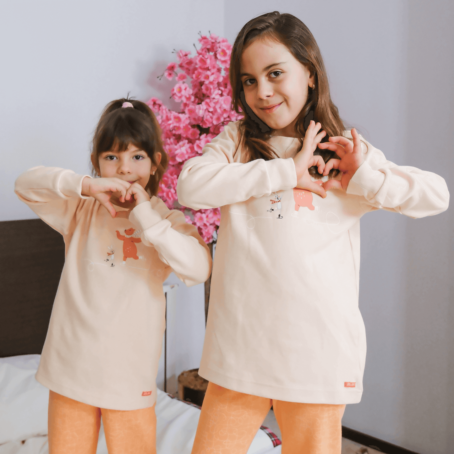 Çocuk ayıcık pijama takımı giyen iki kız çocuğu, sevimli bir ortamda birlikte poz veriyor.