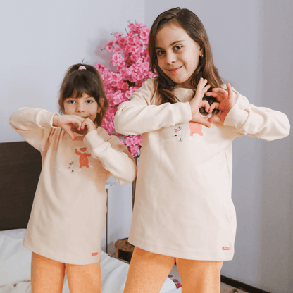 Çocuk ayıcık pijama takımı giyen iki kız çocuğu, sevimli bir ortamda birlikte poz veriyor.