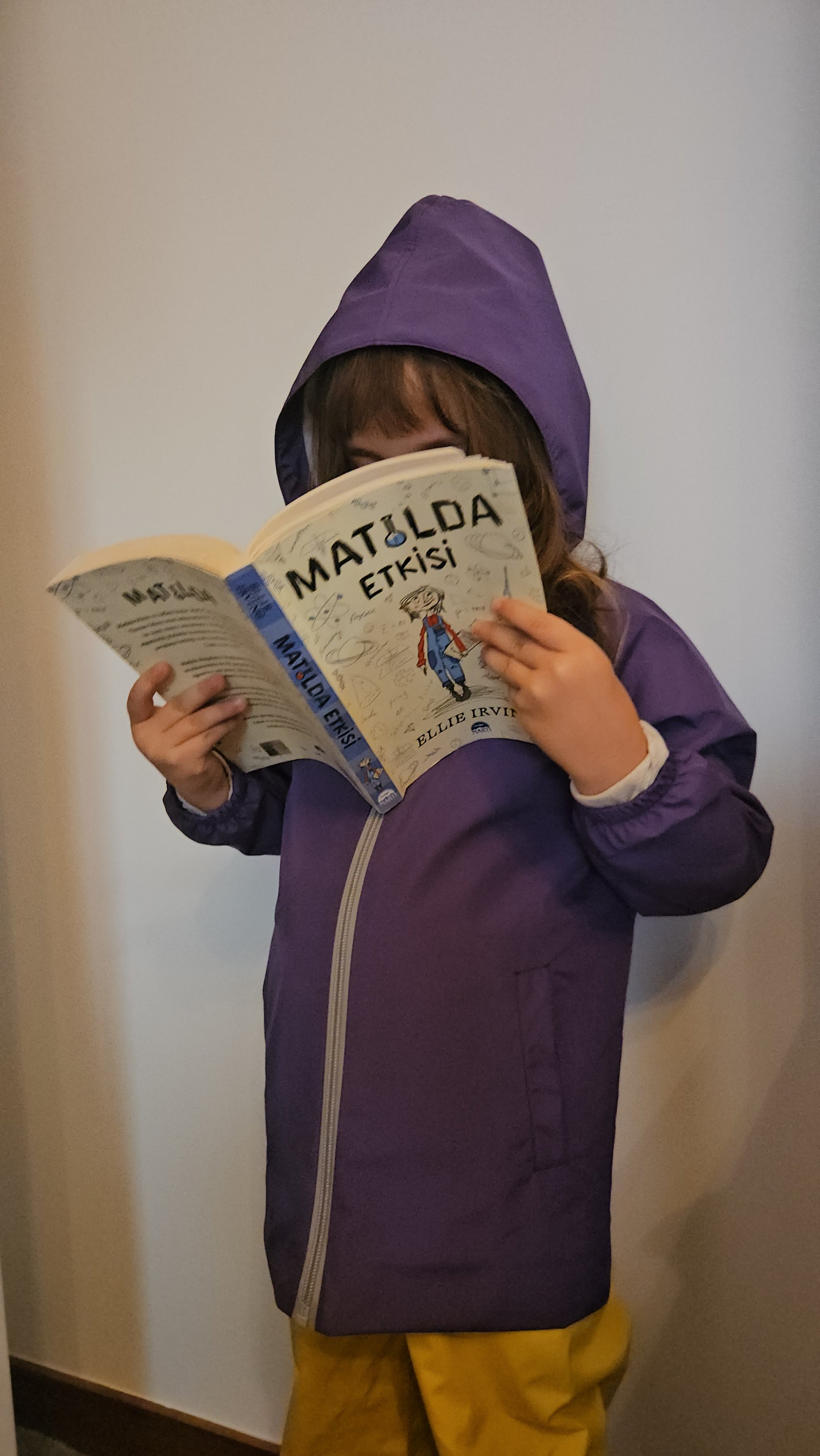 Çocuk Yağmur Ceketi giyen kız, Matilda Etkisi kitabını okurken görünümü.