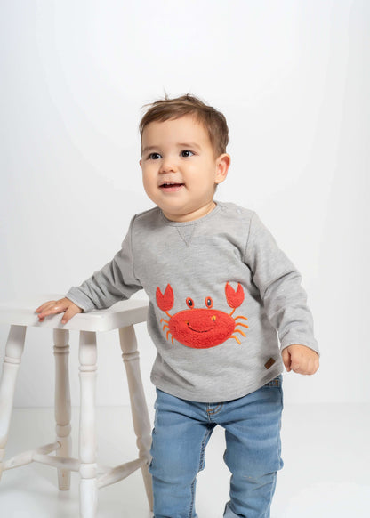Çocuk yengeç nakışlı kazak giyen mutlu bir bebek, yengeç motifi ile eğlenceli bir görünüm sunuyor.
