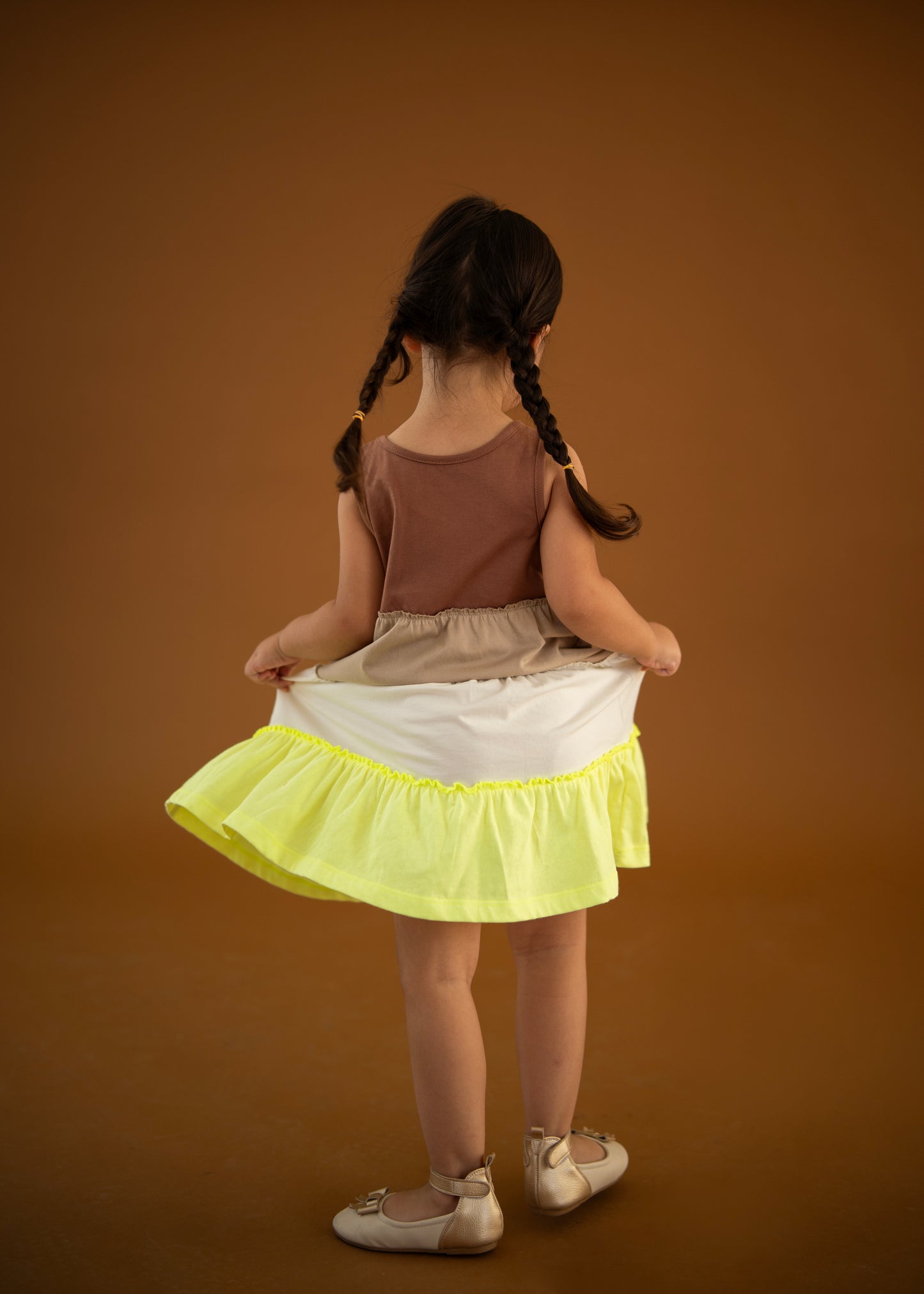 Çocuk, gypsy dress 🌞 giyerken, arkasından poz veriyor, sarı etek ile modern bir görünüm sergiliyor.